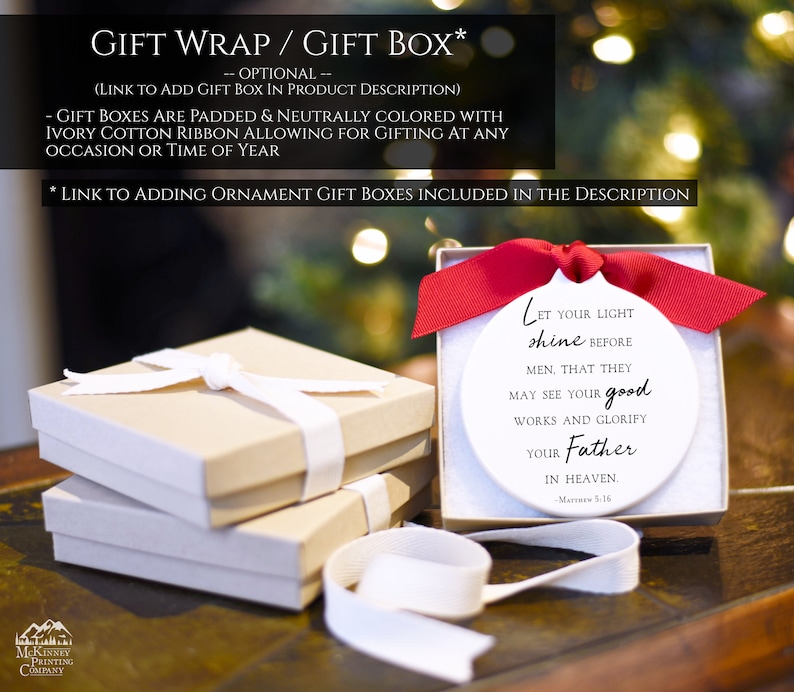 May include: A white ceramic ornament with the text "Let your light shine before men. That they may see your good works and glorify your Father in Heaven. -Matthew 5:16". The ornament is in a white gift box with a red ribbon. The gift box is sitting on a wooden surface.