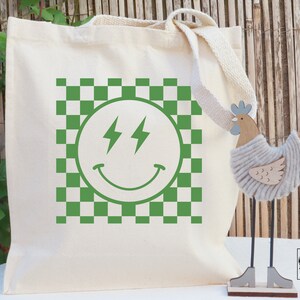 May include: A white canvas tote bag featuring a green checkered pattern and a green smiley face with lightning bolts for eyes. The text "McKinsey Printing Company" is printed in the bottom right corner of the bag.