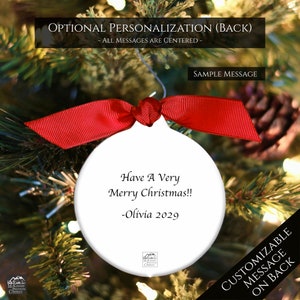 May include: White round Christmas ornament with a red ribbon. The ornament has a personalized message that reads "Have A Very Merry Christmas!! -Olivia 2029".