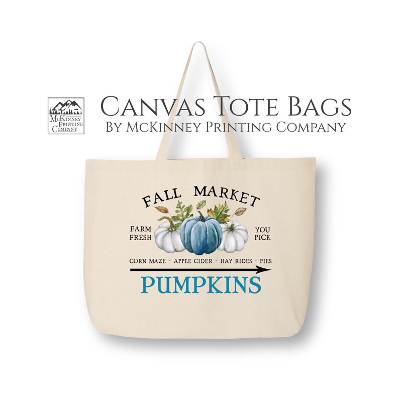 May include: A canvas tote bag with a fall market design. The bag features a blue, white, and green watercolor illustration of pumpkins, leaves, and the text "Fall Market". The text "Farm Fresh" and "You Pick" are also included. The bag has a black arrow pointing to the text "Pumpkins".