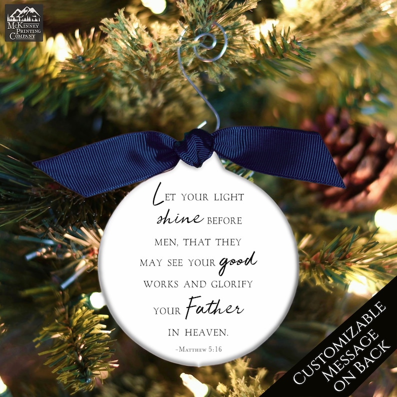 May include: White round Christmas ornament with a blue ribbon. The ornament has a black and white quote from Matthew 5:16, "Let your light shine before men, that they may see your good works and glorify your Father in heaven."