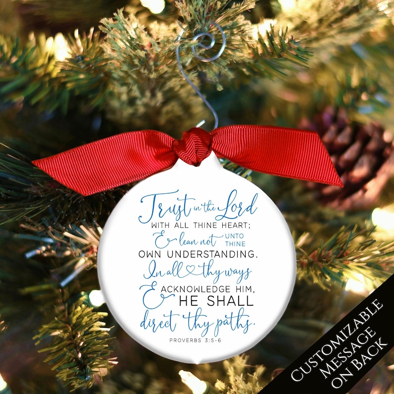 May include: White Christmas ornament with a red ribbon and a silver hook. The ornament has the text "Trust in the Lord" and a Bible verse in blue script. The back of the ornament says "Customizable message on back."