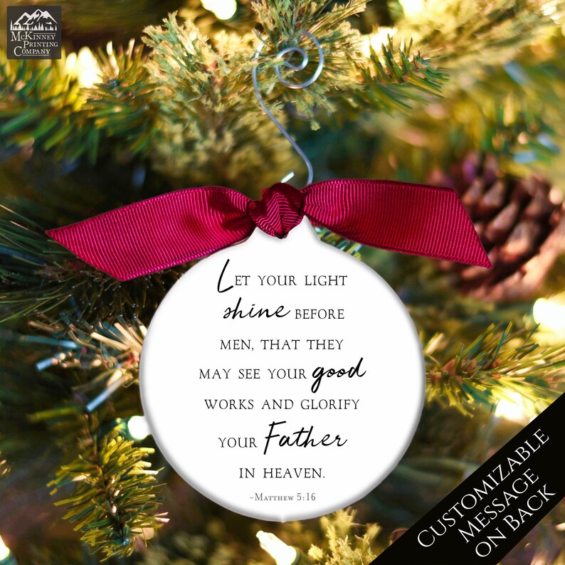 May include: White round Christmas ornament with a red ribbon. The ornament has a quote from Matthew 5:16, "Let your light shine before men, that they may see your good works and glorify your Father in heaven."