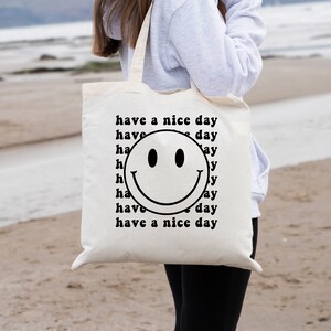 May include: White canvas tote bag with a black smiley face and the text "have a nice day" repeated around the smiley face.
