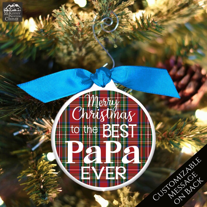 May include: White round Christmas ornament with a red, green, and white plaid pattern. The ornament has the text "Merry Christmas to the Best Papa Ever" in white lettering.