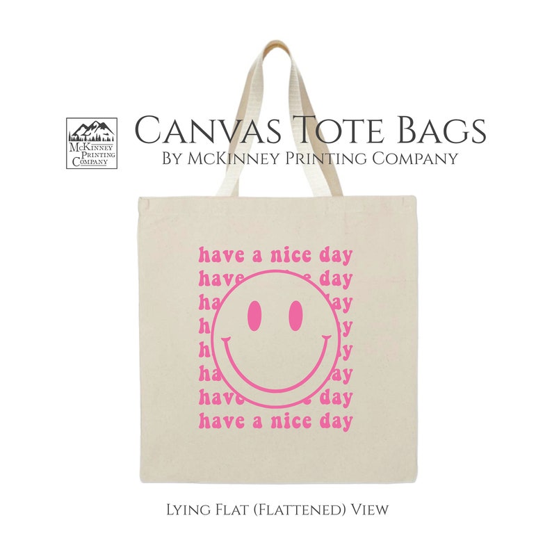 May include: A white canvas tote bag with pink text that says "have a nice day" and a pink smiley face. The bag is lying flat.