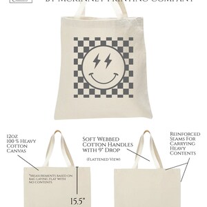 May include: A white canvas tote bag with a black and white chequered pattern and a grey smiley face with lightning bolts. The bag is 15.5 inches tall and 14.5 inches wide. The bag is made of 12 oz 100% heavy cotton canvas with soft webbed cotton handles that have a 9 inch drop. The bag has reinforced seams for carrying heavy contents.