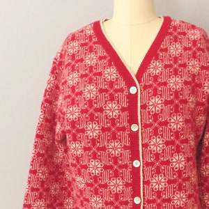 May include: A red and white knitted cardigan with a snowflake pattern. The cardigan has a V-neck and button closure.