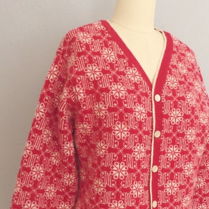 May include: A red and white knitted cardigan with a snowflake pattern. The cardigan has a V-neck and button closure.
