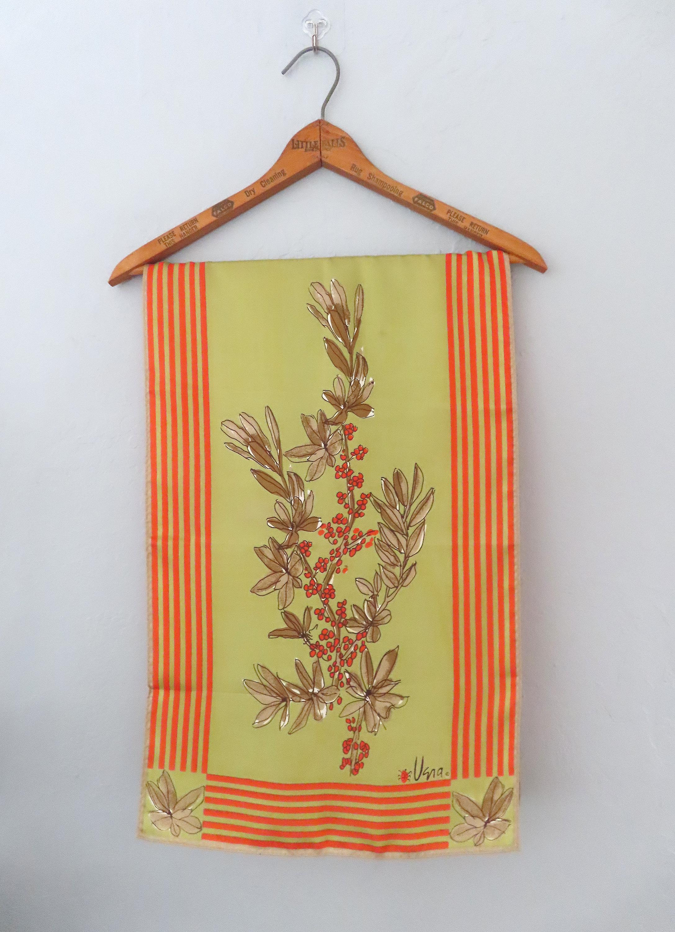 May include: A green silk scarf with orange and yellow stripes and a floral design. The scarf has the word "Uspa." printed on it.