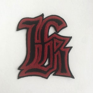 May include: Red and black embroidered iron-on patch of the letter "K" in a gothic font style.