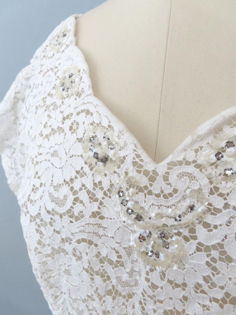 May include: White lace fabric with a V-neckline and beaded embellishments.