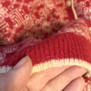 May include: Close-up of a red and white knitted sweater with a white ribbed trim. The sweater has a white knit pattern.