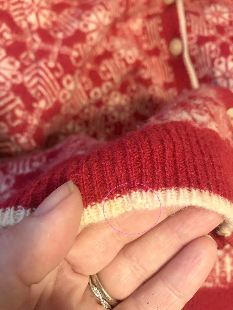 May include: Close-up of a red and white knitted sweater with a white ribbed trim. The sweater has a white knit pattern.