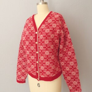 May include: A red and white cardigan with a snowflake pattern. The cardigan has a V-neck and button closure.