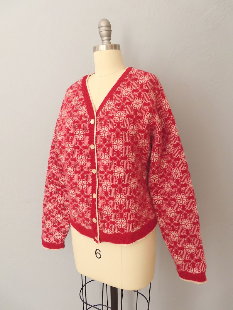 May include: A red and white cardigan with a snowflake pattern. The cardigan has a V-neck and button closure.