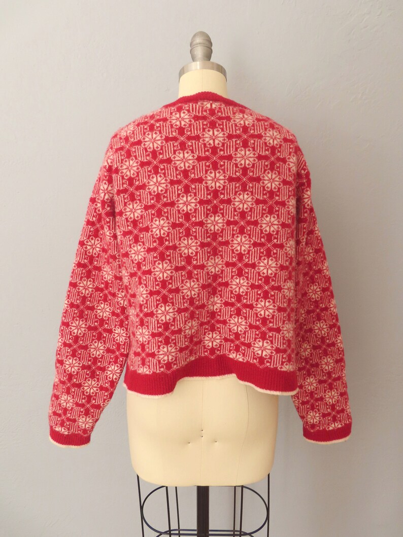 May include: Red knitted sweater with a white geometric pattern. The sweater has a crew neck and long sleeves.