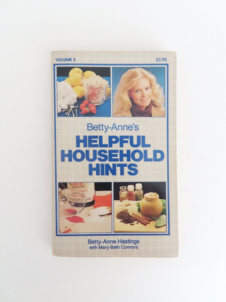 Peut inclure: Couverture d'un livre vintage intitul&eacute; "Betty-Anne's Helpful Household Hints, Volume 2". La couverture pr&eacute;sente des images d'aliments, d'une femme et d'objets m&eacute;nagers. Le titre est en bleu, et le nom de l'auteur est &eacute;galement visible.