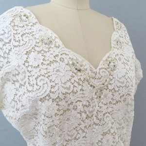 May include: A white lace top with a V-neckline and short sleeves. The neckline and shoulders are adorned with small, sparkly embellishments.