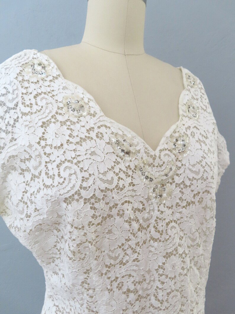 May include: A white lace top with a V-neckline and short sleeves. The neckline and shoulders are adorned with small, sparkly embellishments.
