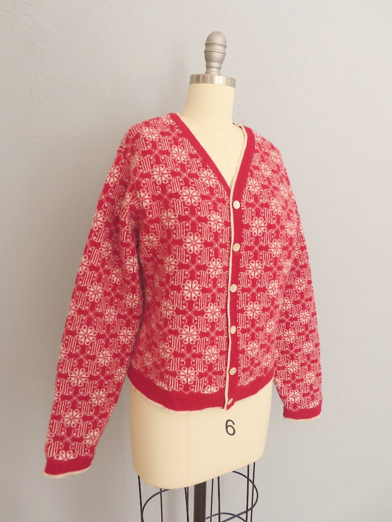 May include: A red and white knitted cardigan with a snowflake pattern. The cardigan has a V-neck and button closure.