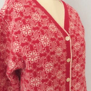 May include: A red and white knitted cardigan with a geometric pattern and button closure.