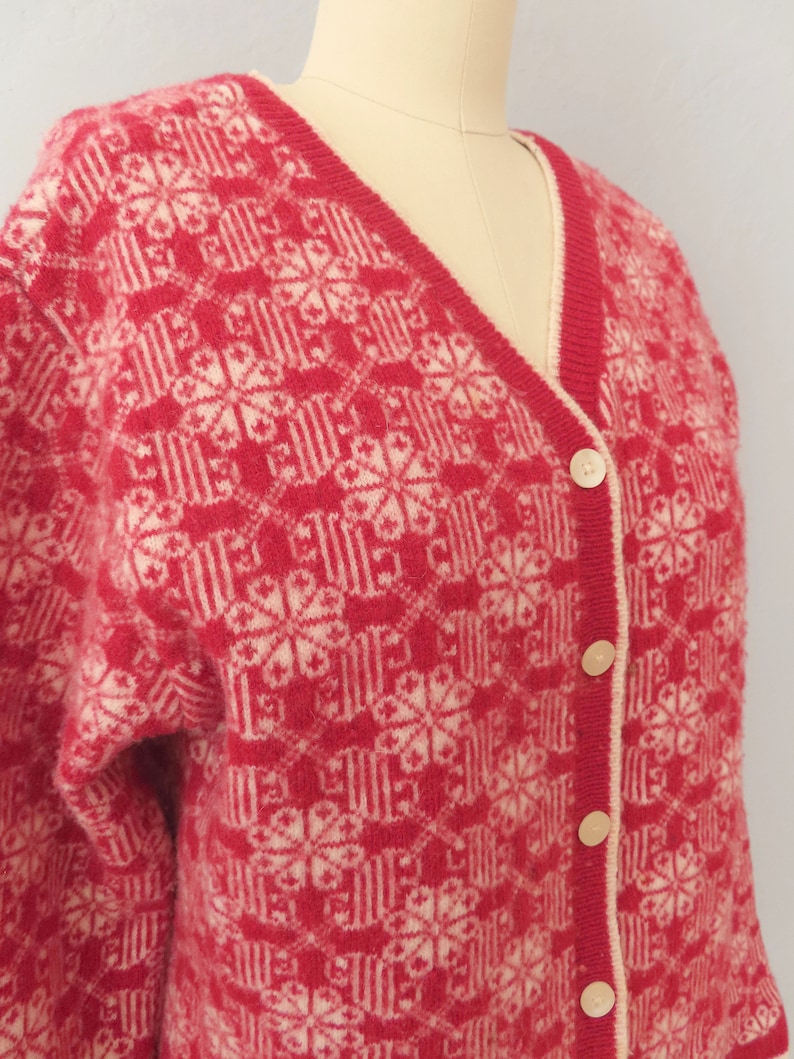 May include: A red and white knitted cardigan with a geometric pattern and button closure.