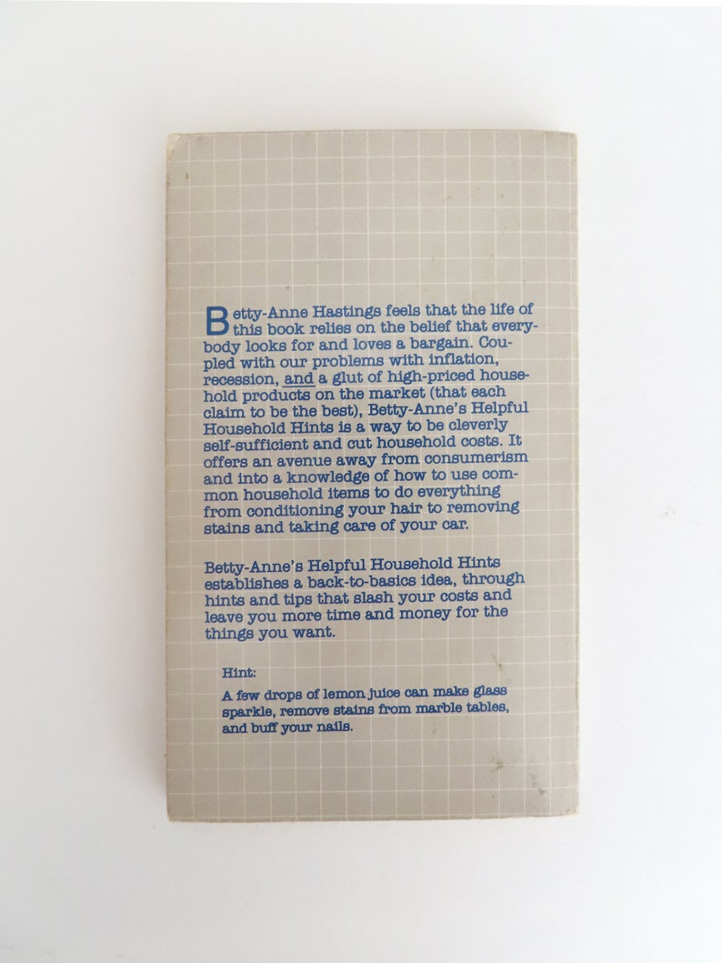 Peut inclure: Dos de livre vintage, "Betty-Anne's Helpful Household Hints". La couverture grise clair &agrave; motif quadrill&eacute; pr&eacute;sente du texte bleu. Le texte d&eacute;crit les astuces de l'ouvrage pour &eacute;conomiser &agrave; la maison.