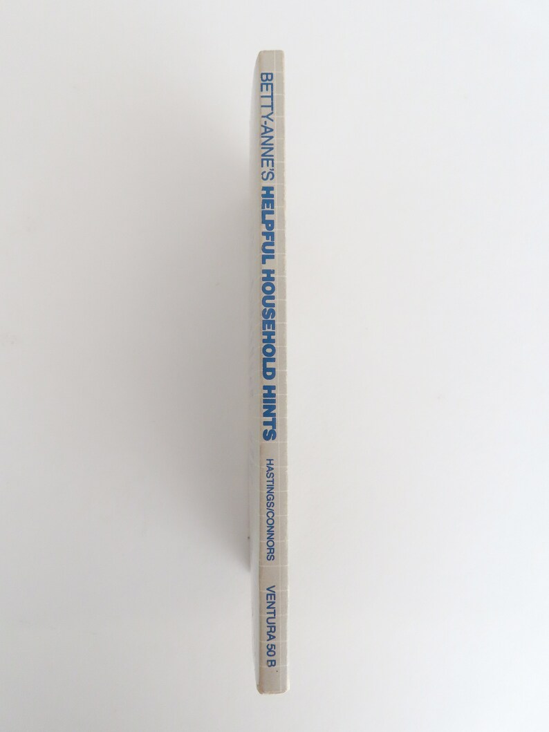Peut inclure: Tranche de livre vintage avec le titre "Betty-Anne's Helpful Household Hints" en bleu. Le nom de l'auteur, Hastings/Connors, et "Ventura 50 B" sont &eacute;galement imprim&eacute;s sur la tranche. Le livre est pos&eacute; sur un fond blanc uni.