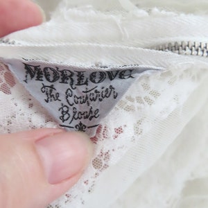 May include: White lace blouse with a white tag that reads "Morelove The Couturier Blouse".
