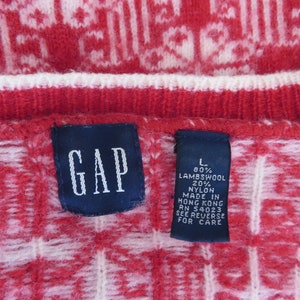 May include: A red and white sweater with a geometric pattern. The sweater is labeled "GAP" and has a size tag that reads "L 80% Lambswool 20% Nylon Made in Hong Kong RN 54023 See Reverse for Care."
