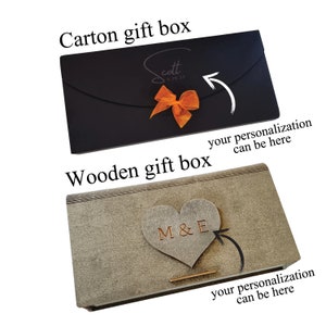 May include: Two gift boxes, one black cardboard and one wooden. The cardboard box has a bow and the text "cott 4.29.23" on it. The wooden box has a heart with the text "M&E" on it. Both boxes have space for personalization.