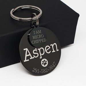 May include: Black metal dog tag with the name Aspen engraved on it. The tag also includes the text "I am microchipped" and a phone number.
