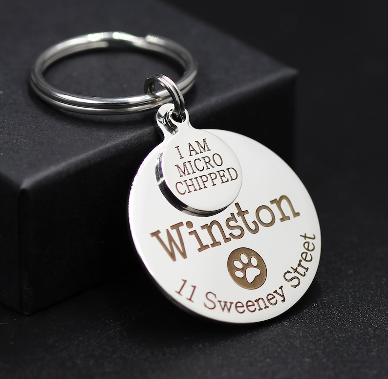May include: Silver dog tag keychain with a paw print and the text "Winston 11 Sweeney Street" and a smaller tag that says "I am microchipped".