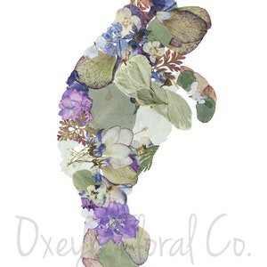 May include: A manatee silhouette created with pressed flowers and leaves. The flowers are in shades of purple, blue, white, and green.
