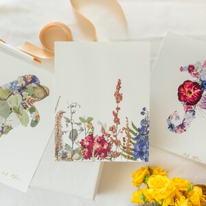 May include: Three framed prints with pressed flower art. The prints feature a manatee, a floral arrangement, and a seahorse. The prints are on white backgrounds and have a gold signature in the bottom right corner.
