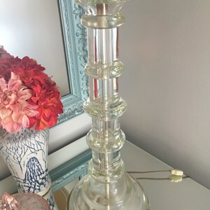 K&ouml;nnte beinhalten: Eine klare Glastischlampe mit runder Basis und zylindrischem Schaft. Die Lampe hat einen Messingfu&szlig; und einen klaren Glasschirm.