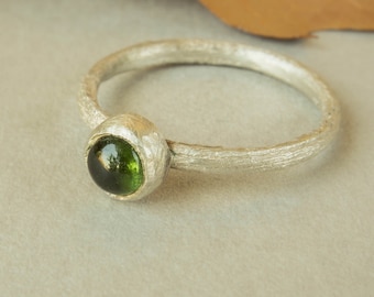 May include: A silver ring with a textured band and a green gemstone set in a bezel setting.