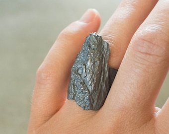 May include: A silver ring with a textured, rough, and irregular design. The ring is made to look like a piece of rock.