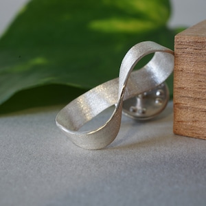 May include: A silver infinity symbol pendant with a brushed finish. The pendant is made of metal and has a smooth, rounded shape.