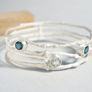 May include: Silver bangle bracelet with three gemstones. Two blue gemstones and one clear gemstone are set in the silver.