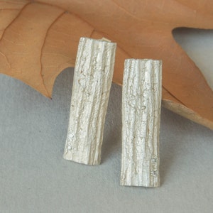 Puede incluir: Un par de pendientes de plata con forma de corteza de árbol con pequeños detalles de diamantes.