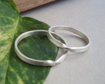 May include: Two silver rings, one twisted, on a green leaf. The rings are simple and elegant.