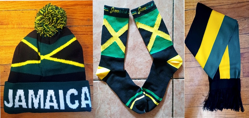 May include: A set of Jamaican themed accessories including a black and green beanie with a yellow pom pom and the word "Jamaica" in white lettering, a pair of black socks with a yellow, green, and black Jamaican flag design, and a black and yellow striped scarf with green stripes and black tassels.