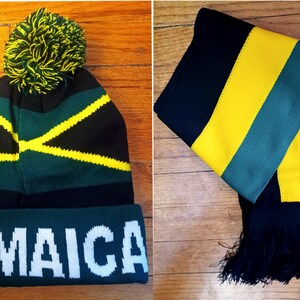 May include: A black, green, and yellow knit beanie with a pom-pom on top and the word "JAMAICA" written in white on the front. A matching black, green, and yellow striped scarf with black fringe.