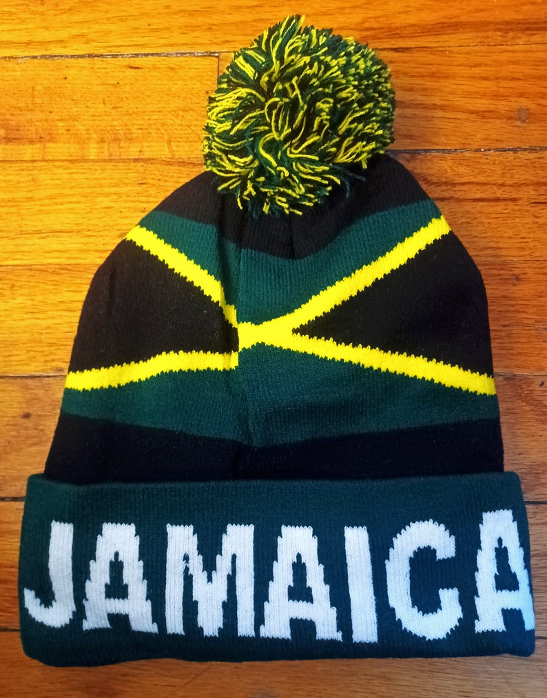 May include: A black, green, and yellow knit beanie with a pom pom on top. The beanie has the word "JAMAICA" written in white on the bottom band.