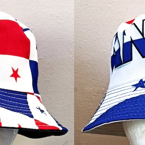 May include: A white bucket hat with a red, white, and blue checkered pattern and a blue star on the front. The hat also has the word "PANAMA" written in black letters on the front.