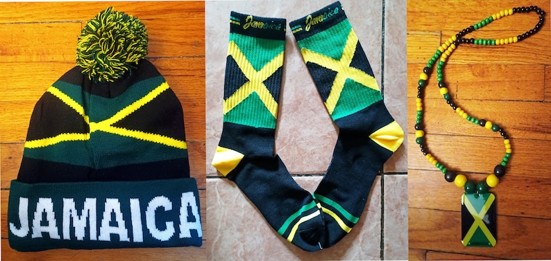 May include: A set of three Jamaican themed accessories: a black and green beanie with a yellow pom-pom and the word "JAMAICA" in white, a pair of black socks with yellow and green stripes and the word "Jamaica" in yellow, and a black and brown beaded necklace with a yellow and green pendant featuring the Jamaican flag.