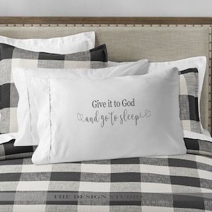 May include: White pillow with black text that reads "Give it to God and go to sleep" with a heart on each side of the text. The pillow is on a black and white checked bedspread.