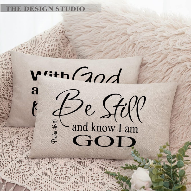 Pu&ograve; includere: Due cuscini beige con testo nero. Il cuscino superiore dice "With God" e il cuscino inferiore dice "Be Still and know I am GOD" con il riferimento biblico "Psalm 46:10" sotto.